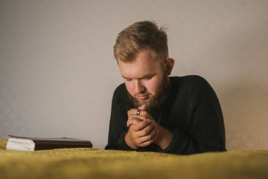 Man kneeling in prayer by his bedside A man praying next to his Bible.
