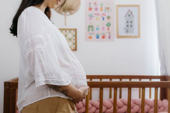 Pregnant woman A pregnant woman happily stands in the nursery she's prepared for her newborn.