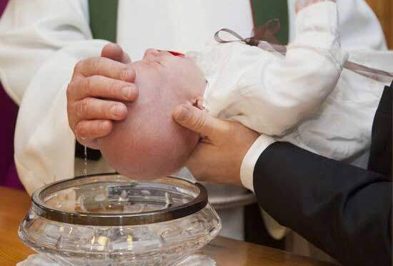 A priest sprinkling water on a baby's head during infant baptism