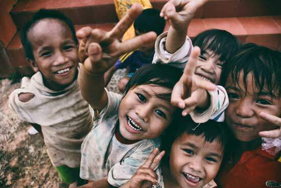 A group of children smile as they show peace signs with their hands.