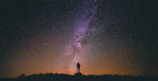 Silhouette of a woman looking up at the milky way in the starry night sky A person stands on a hill at night and gazes into a sky filled with stars