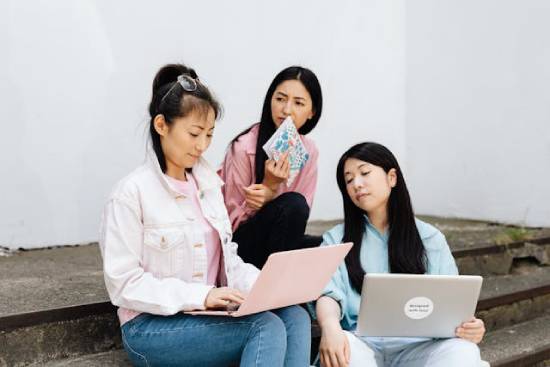 Three Asian women sitting on steps Three women talking about spiritual gifts as they research the subject on their laptops