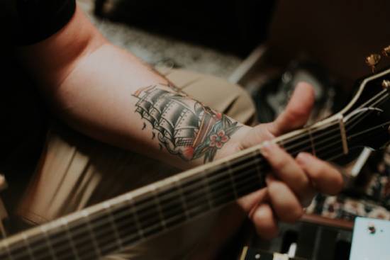 A man, with a tattoo on his forearm, playing the guitar.