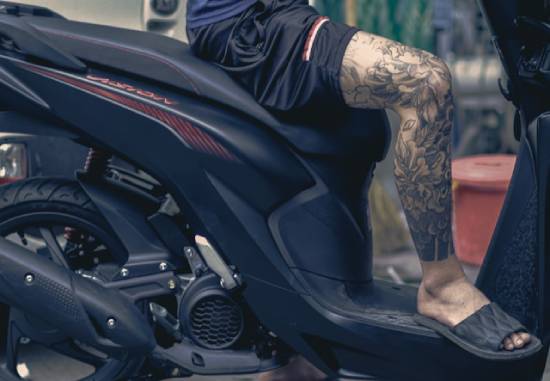 A man on a motorcycle with tattoos on his leg.