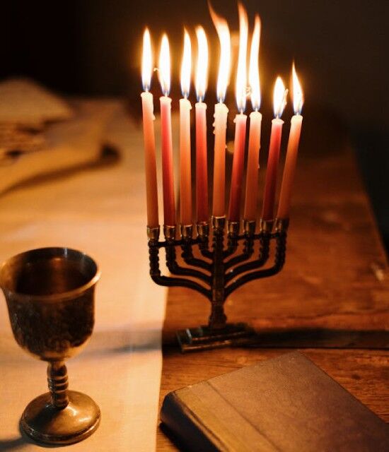 Menorah with lit candles on a wooden table at evening A menorah with lit candles on a table next to a drinking cup illustrates Jewish celebrations.
