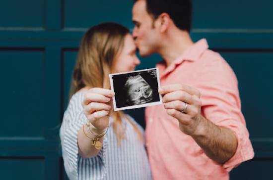 A couple in the background happily holds up a sonogram in the foreground.