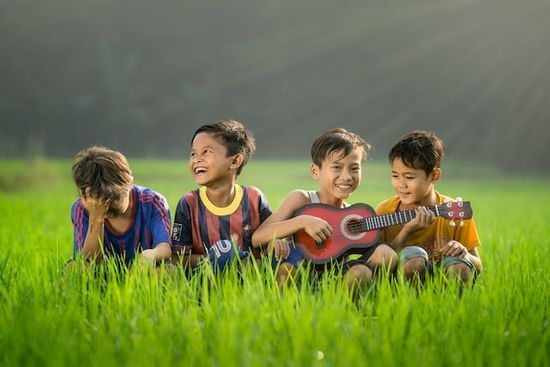 Playing Ukulele at Camp Four boys playing ukulele in a field at summer camp