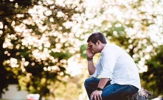 A man sitting on a tree stump, hand covering his face in shame.