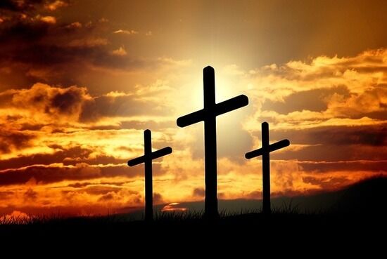 The silhouettes of three crosses stand in front of the setting sun.