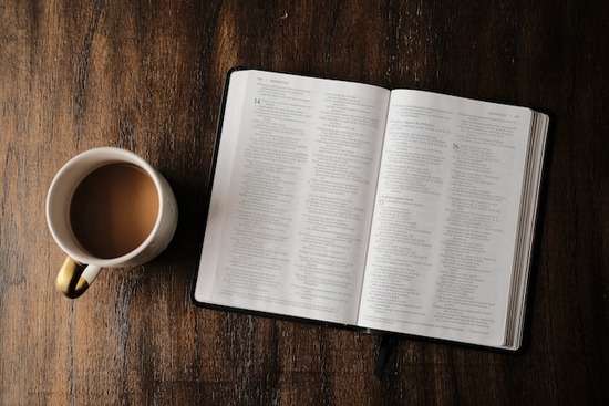 A Bible on a table next to a coffee mug