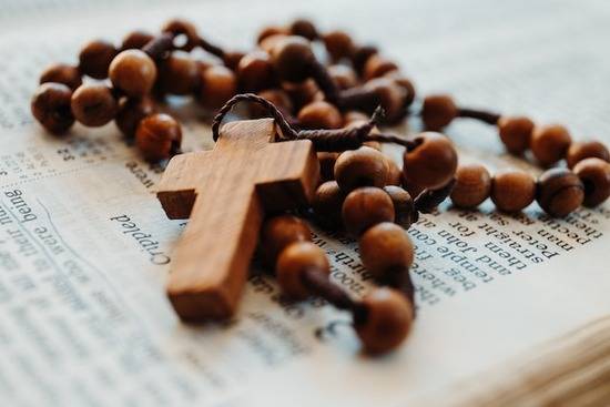 Rosary beads and a wooden cross on top of an open Bible A rosary and a cross