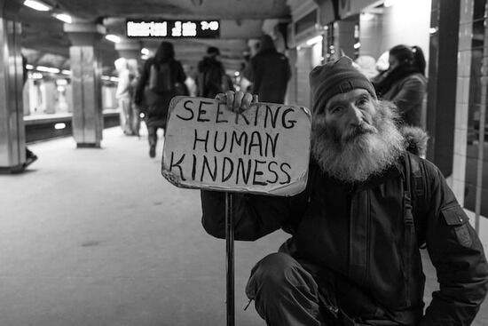 A homeless man holding a sign asking for kindness