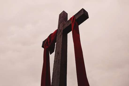 A red sash hangs on a wooden cross, representing the cross Jesus died on.