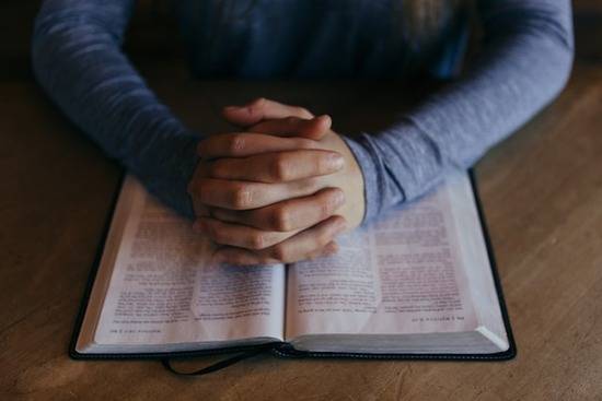 Folded Hands on Bible A man folding his hands in prayer over a Bible.
