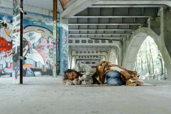 Homeless Man Sleeping on Ground A homeless man sleeping on the ground under a bridge