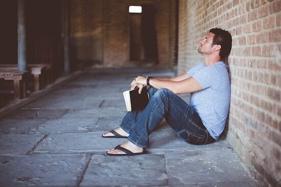 Man Sitting with Bible A man sitting against a wall, holding his Bible, and praying