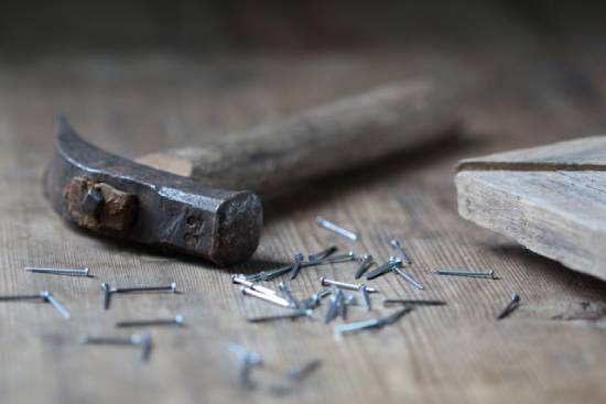 A hammer rests on a wooden floor amidst a pile of nails