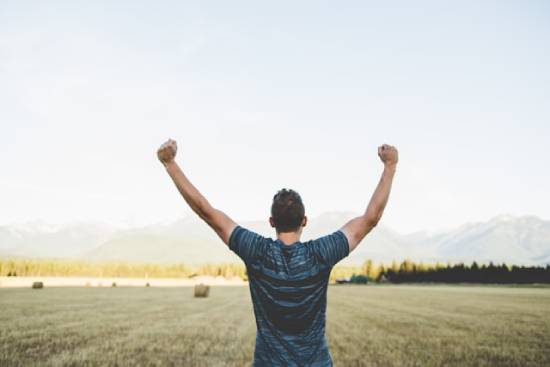 Man Overlooking a Hay Field Raising his Hands in Victory A man in a field with his arms triumphantly raised, illustrating the victory we can experience with God on our side.
