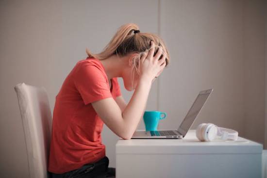 A woman sitting at a desk anxiously looks at her laptop screen, depicting how worrying can affect us.
