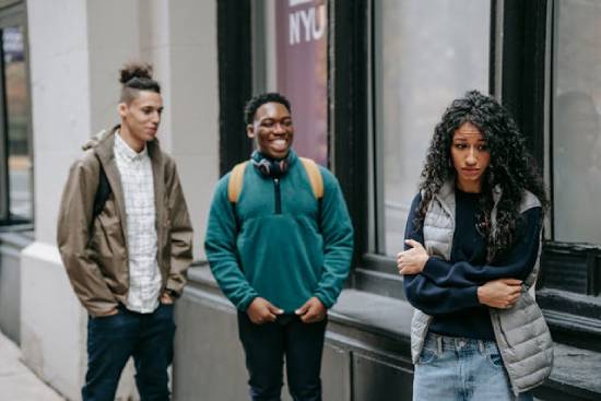 A young woman holds herself while two guys laugh at her, showing how painful rejection can sometimes be.