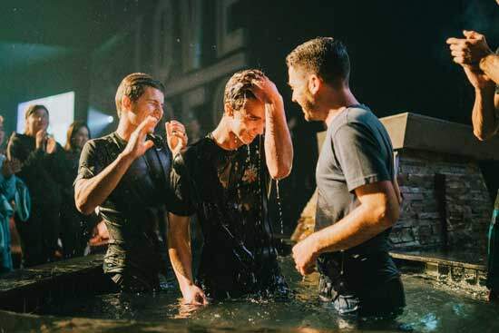 Young Man Getting Baptised Two men in a baptismal tank, having just baptized a third man