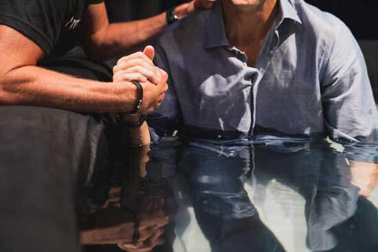Man Baptism A pastor lowers a man into a tub filled with water to baptize him.