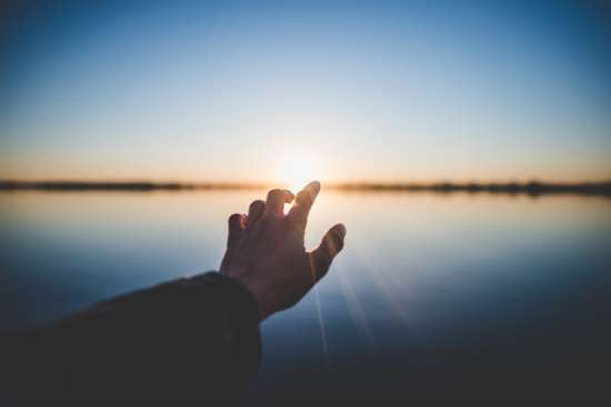 Hand reaching out to the sun A hand reaching out toward the sun that is on the horizon beyond a lake