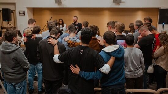 Young adults in prayer Christian young adults gathered with arms around each other for prayer