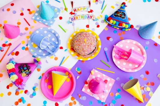 Birthday party decorations and confetti on a table A table covered in pink and purple birthday party favors, hats, and confetti