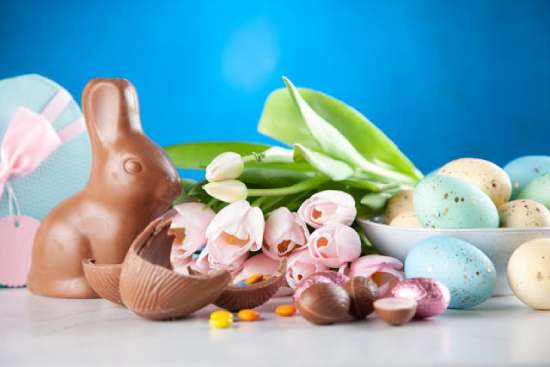 Chocolate easter bunny, chocolate eggs, and painted easter eggs on a table Chocolate Easter bunnies and candy with flowers and birds' eggs
