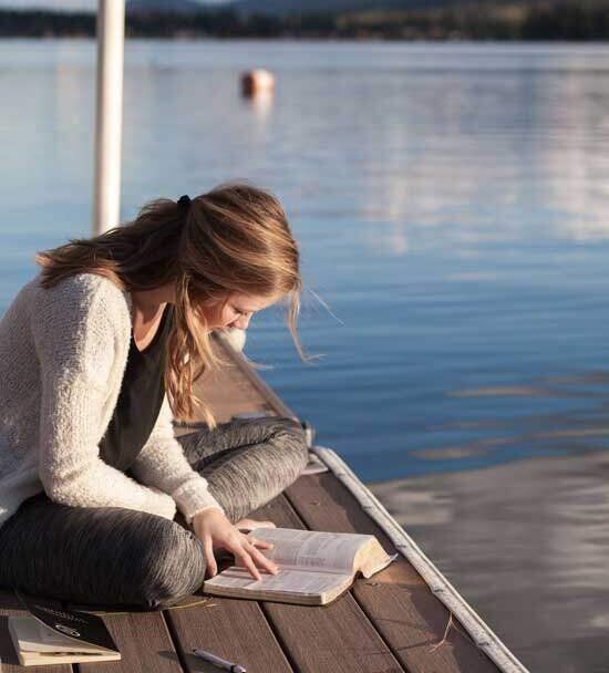 Woman reading Bible Woman sitting at the shore of a lake, daily feeding on the Word of God, the Bible
