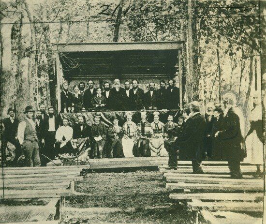 Camp meeting in 1875 James and Ellen White with other Adventists under a canopy at a camp meeting in 1875