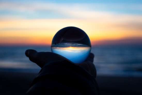 Glass ball and sunset signifying the future Hands holding a glass ball that is reflecting the ocean and the sunset