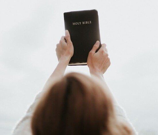 woman holding out a Bible A woman clutching a Bible with both hands and lifting it up