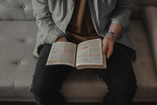 Reading Bible on Couch Sitting down with the Bible will help us better understand God's grace and love.