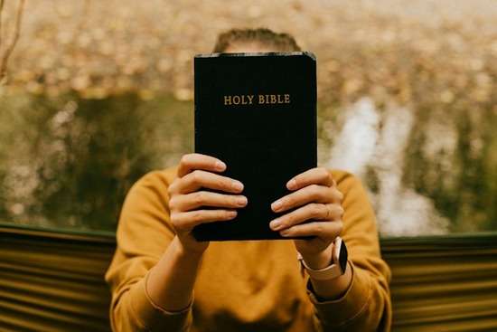Woman holding up a copy of the Bible A woman holding up a Bible in front of her face