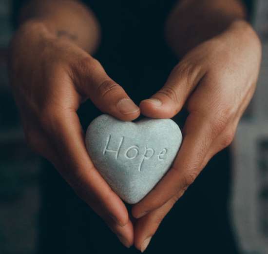 Hope Rock Hands holding a heart-shaped rock with the word Hope etched into it