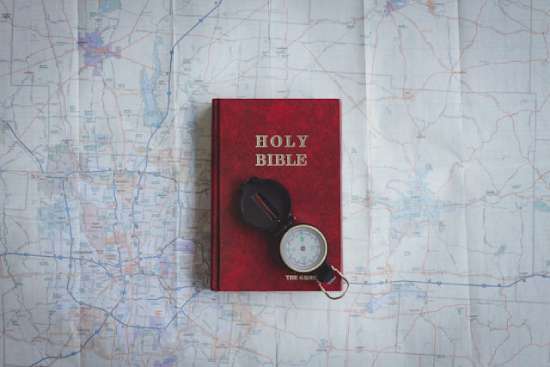Bible with Map and Compass A red Bible and compass on top of a map, symbolizing how the Bible is our guide