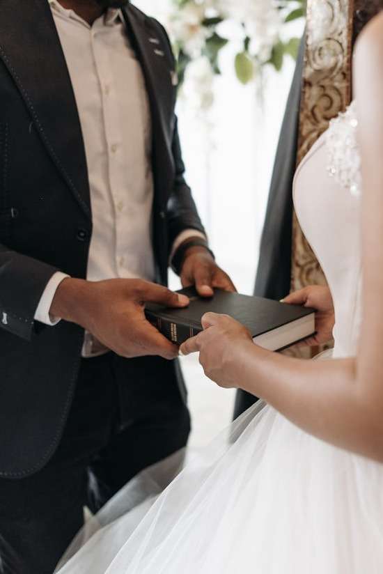 Bride and groom holding BIble A bride and groom facing each other and holding onto a Bible that's between them