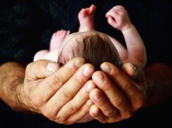 Hands Holding a Baby An infant child resting in their parent's hands.