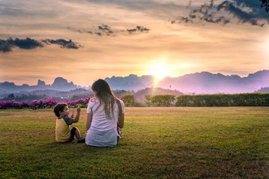 Woman and Son in Nature A mother sits in a field with her young son, attentively watching as he shows her something he found.