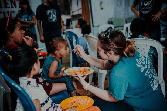Missionary Helping Poor A woman feed a spoonful of food to a impoverished child