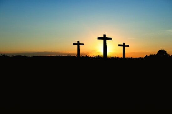 Three crosses stand near each other underneath a sunset sky. 