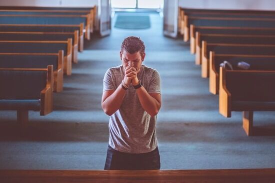 A Christian man kneels at the front of a church to pray