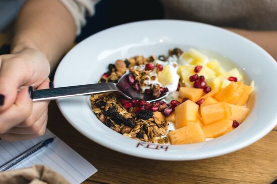 Nutritional Breakfast A hand holding a spoon and eating granola with fresh berries and cantaloupe, components of a healthy lifestyle