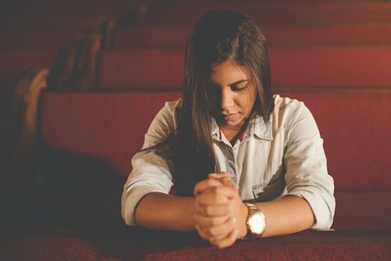 Woman Praying A girl sitting in a church pew, folding her hands and closing her eyes in prayer.