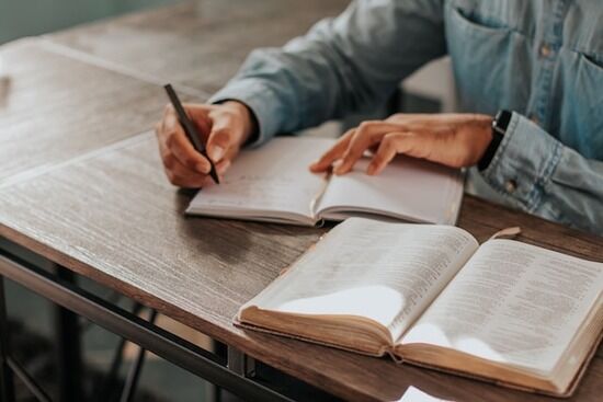 Bible Study A person taking notes in a journal as they study the Bible