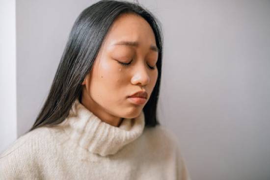 A woman with her eyes closed, with a tear running down her cheek.