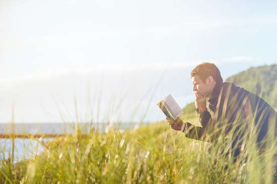 A man sitting near a lake, reading the Bible
