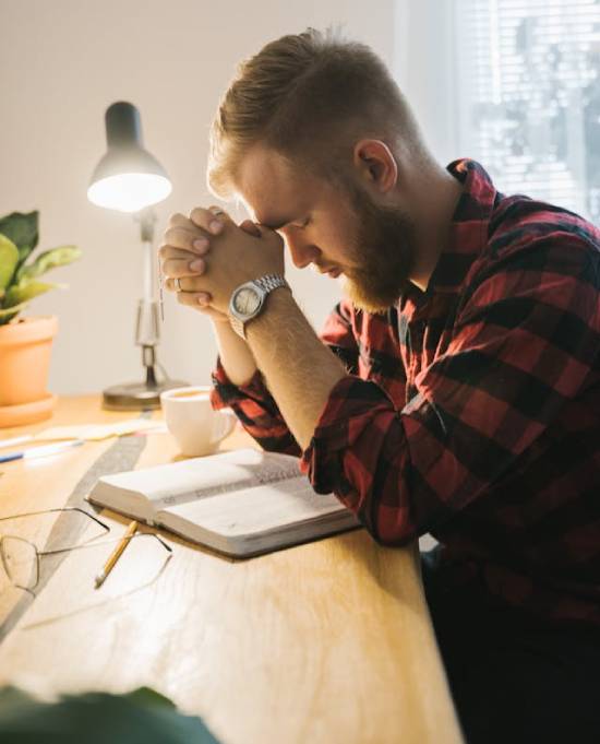 A man sitting at his desk praying over a Bible.